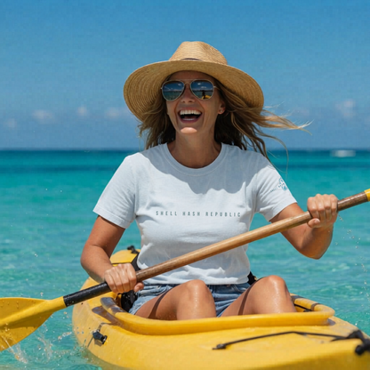 Woman in a straw hat and sunglasses paddling a yellow kayak in clear blue water, wearing a Shell Hash Republic Comfort Colors T-Shirt with a logo