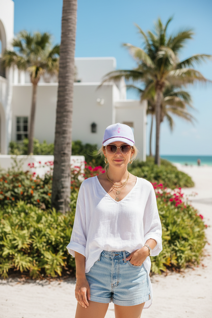 Woman wearing a Shell Hash Republic Small Fit Women's Hat by Imperial, white shirt, and denim shorts on a sunny beach
