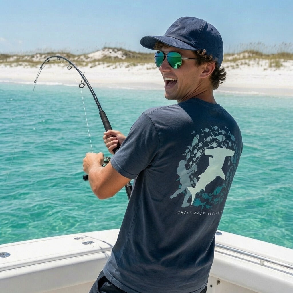 Man fishing from a boat wearing a Shell Hash Republic Comfort Colors China Blue T-Shirt with a Fish-On retro graphic tee design