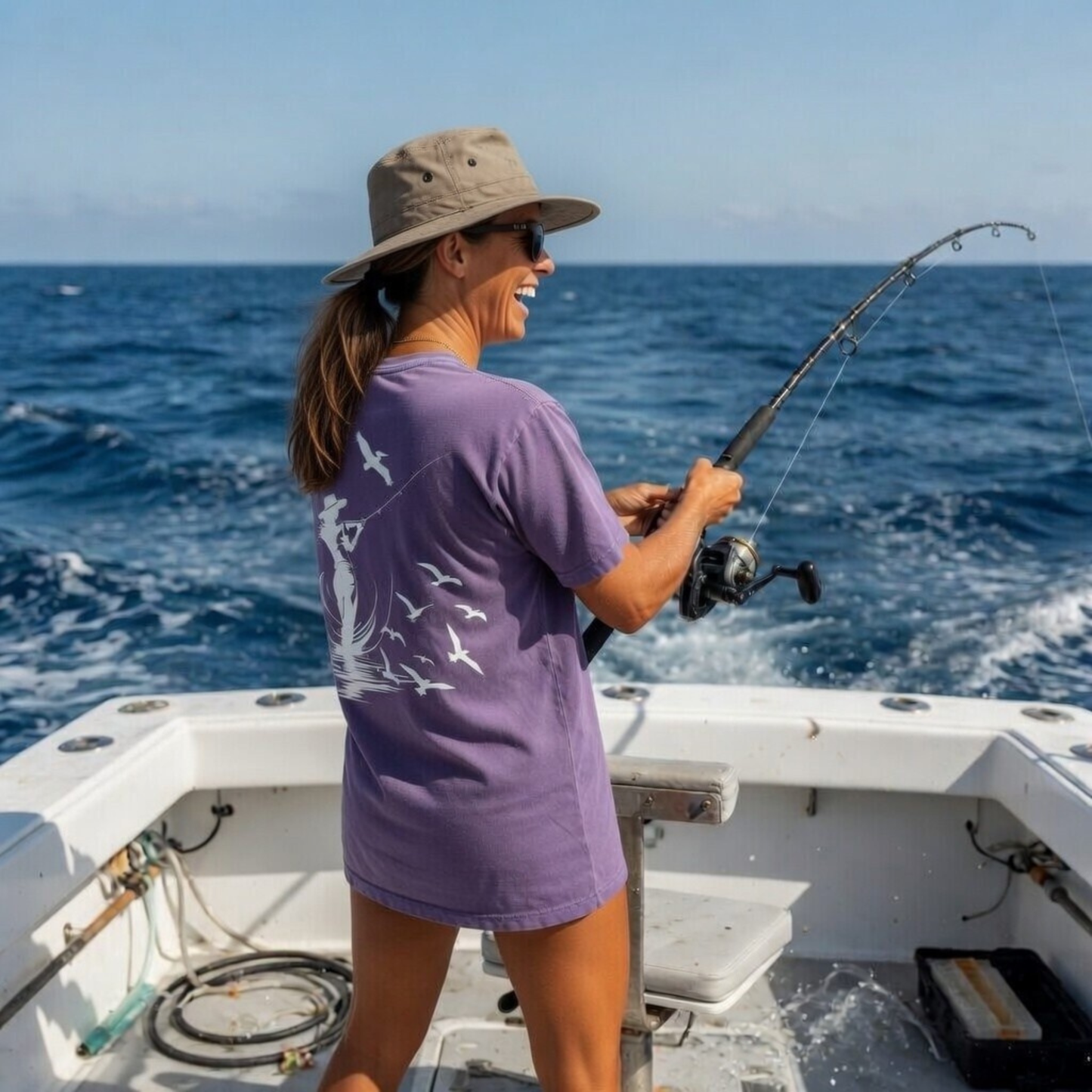 Woman in Shell Hash Republic Comfort Colors Wine T-Shirt fishing from a boat, with a Sunset Sail graphic on the back