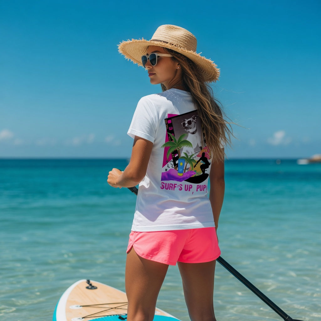 Woman in Shell Hash Republic Comfort Colors T-Shirt with Surfs Up Pup graphic, straw hat, and sunglasses, standing on a paddleboard in clear blue water