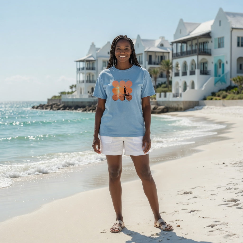Woman on beach wearing Shell Hash Republic Comfort Colors T-Shirt with Sunset Paddle graphic