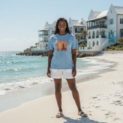 Woman on beach wearing Shell Hash Republic Comfort Colors T-Shirt with Sunset Paddle graphic