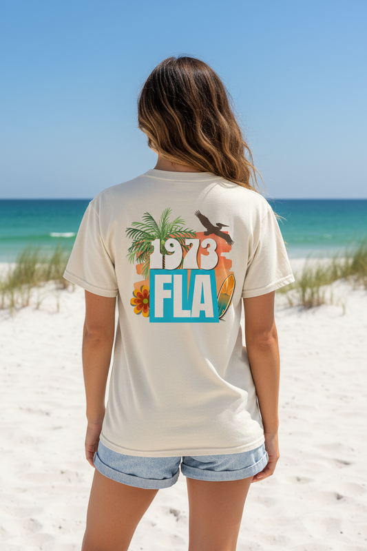 Shell Hash Republic Ivory Comfort Colors T-Shirt with 1973 Surf retro graphic tee design on a woman at the beach