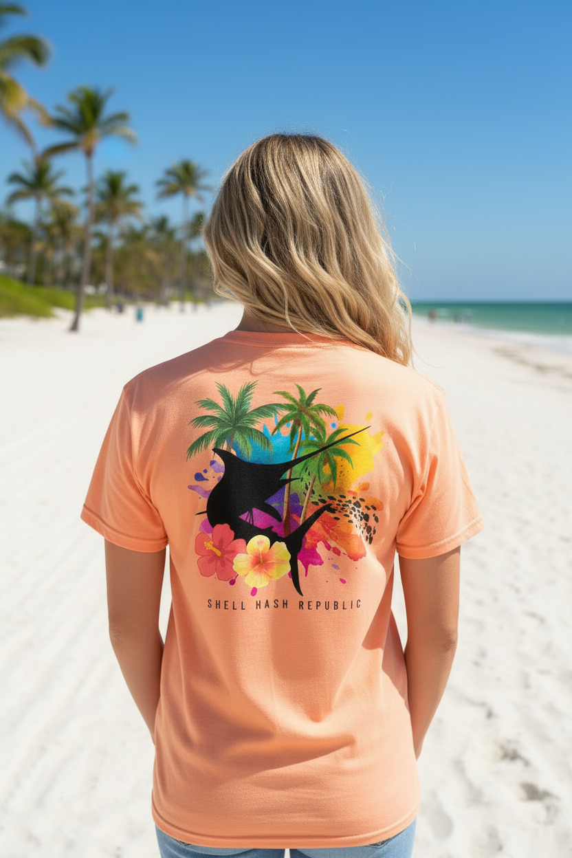 Woman in Shell Hash Republic Comfort Colors T-Shirt with Marlin Splash Tropical Back Print, Swordfish Splash Collage, on a beach